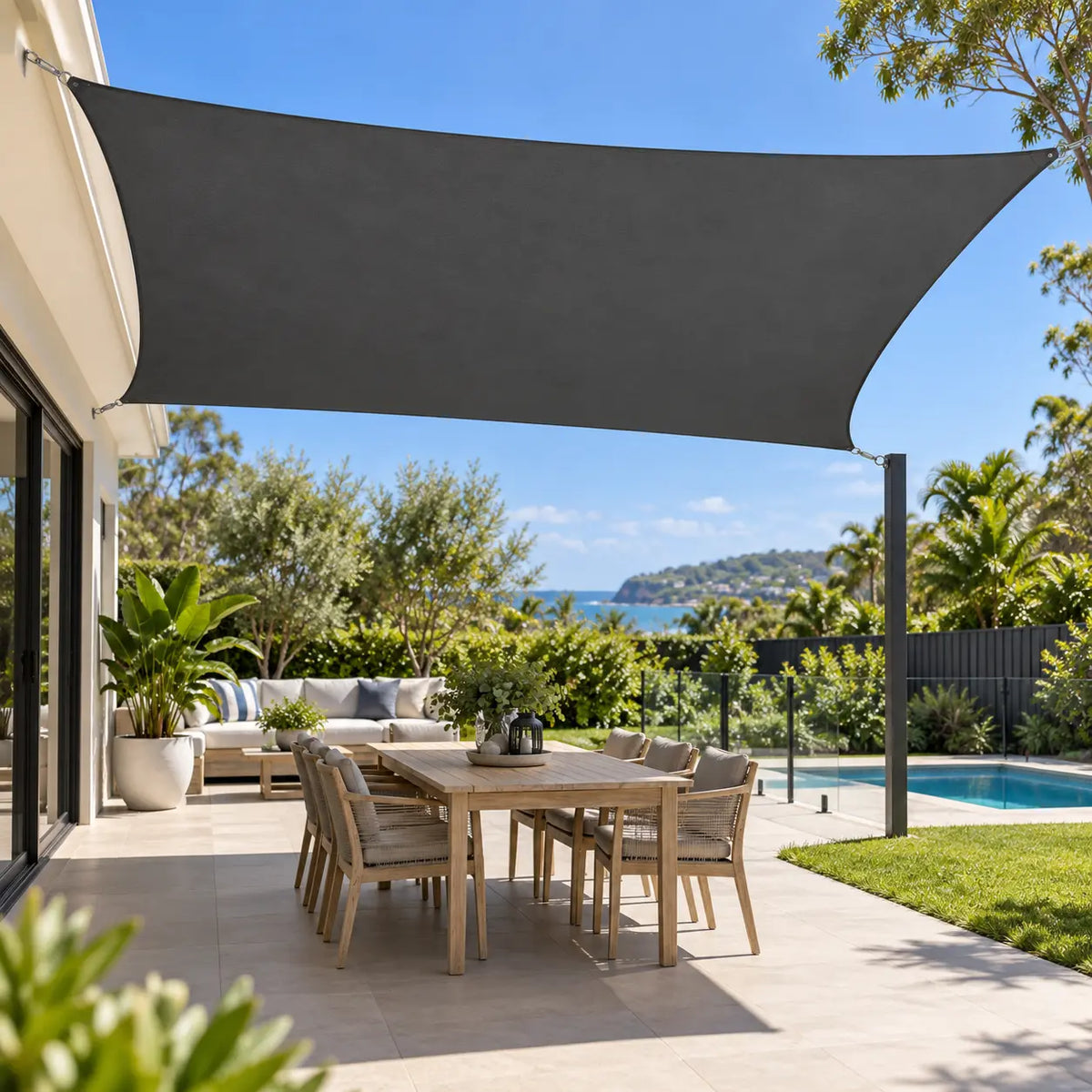 Shade sail anthracite rectangle over outdoor dining table and chairs beside pool in Australian coastal garden