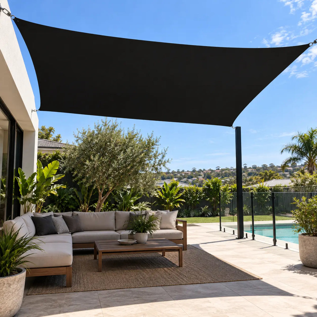 Black shade sail rectangle over outdoor lounge sofa and coffee table beside pool in Australian backyard