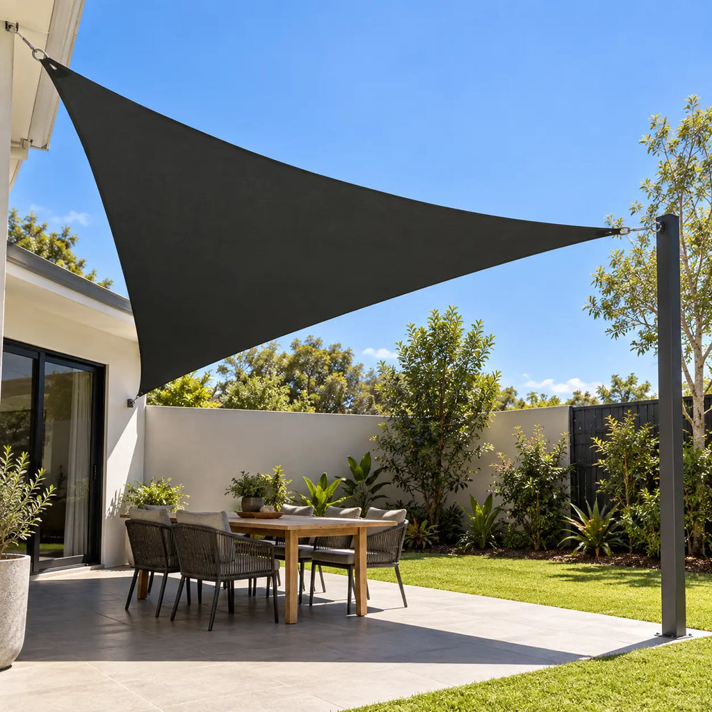 Anthracite triangular shade sail over outdoor dining table with rope chairs in Australian backyard with tropical garden