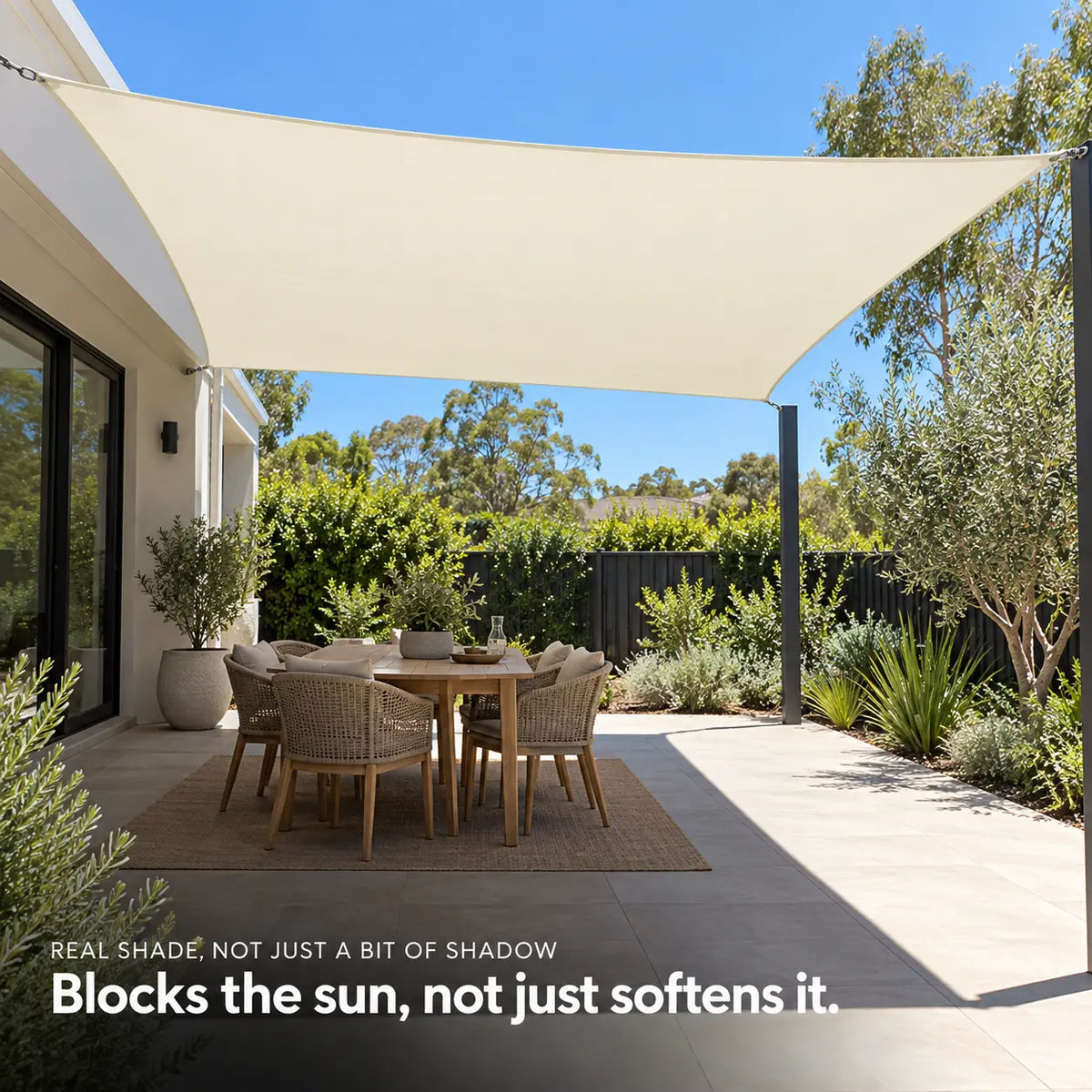 Cream shade sail UV protective rectangle blocking full sun over outdoor round dining table with rattan chairs and native garden Image