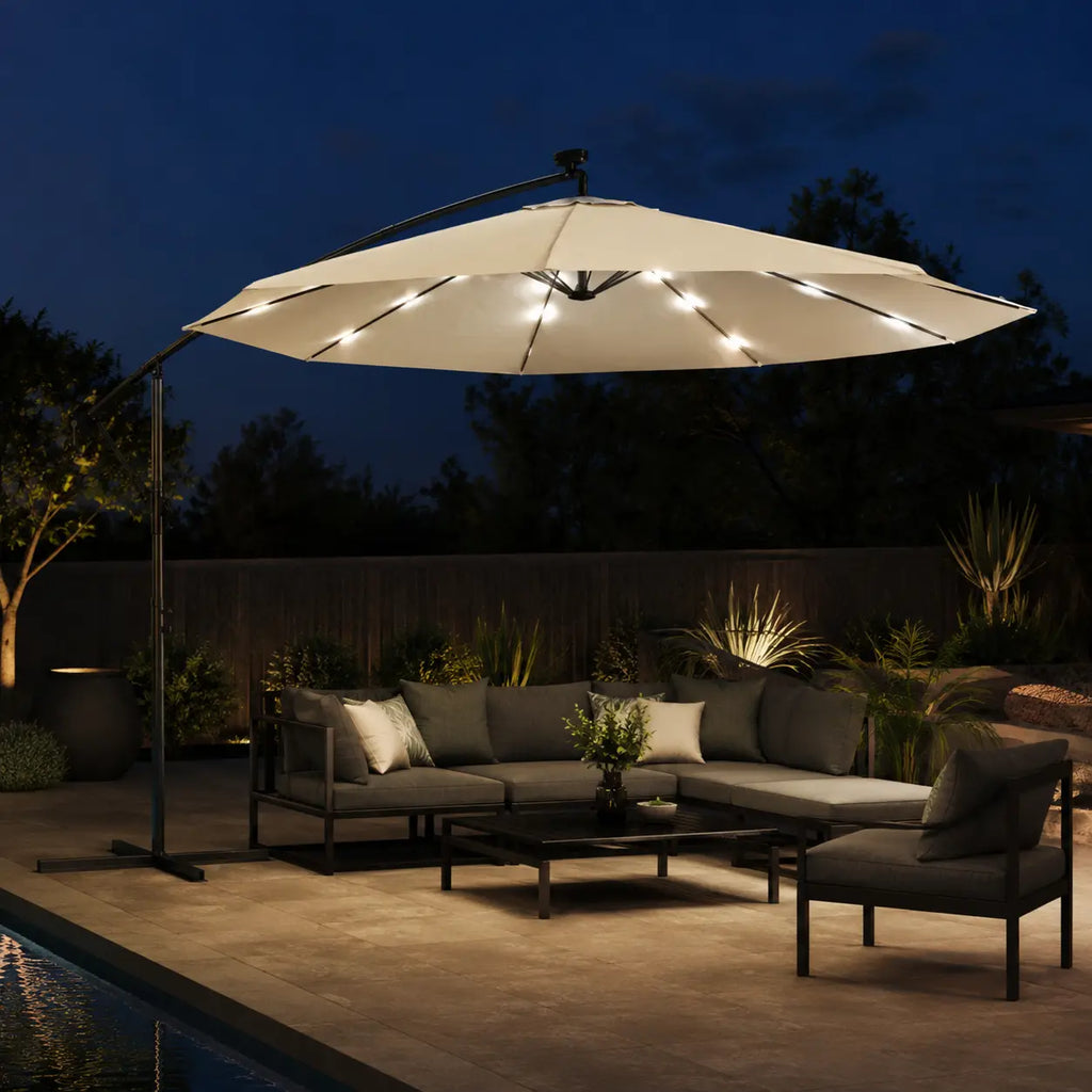 Round cantilever umbrella 3m Sand with solar LED lights on over outdoor lounge beside pool at night – Solano