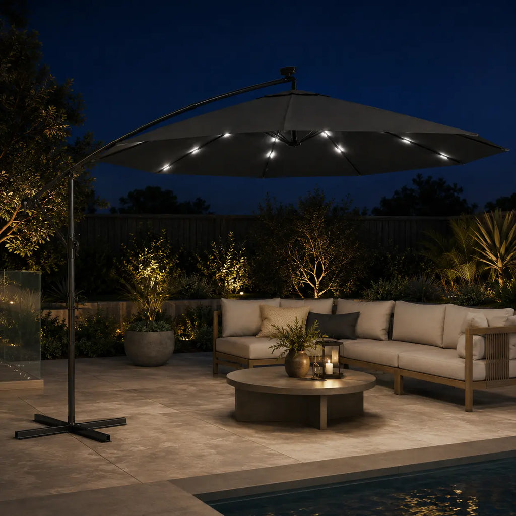 Round cantilever umbrella 3m Anthracite with solar LED lights on over outdoor lounge beside pool at night – Libeccio