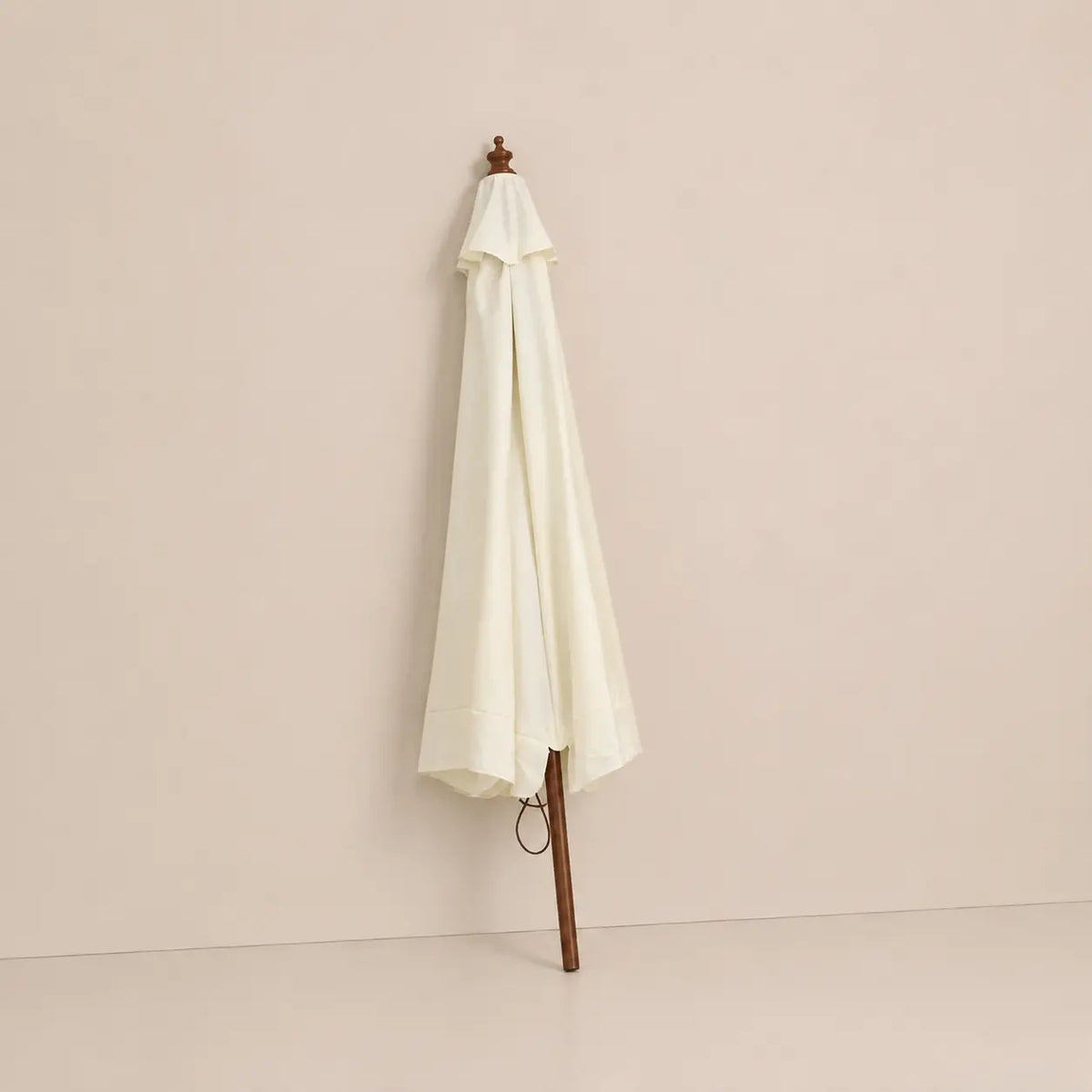 Sand white market umbrella folded closed with hardwood pole and carved wooden finial