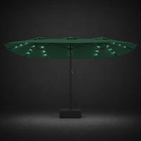 Green double canopy market umbrella with integrated LED lights illuminated at night on a dark background