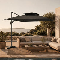 Anthracite cantilever umbrella 3x3m with vented double canopy shading an outdoor lounge setting at sunset by the sea