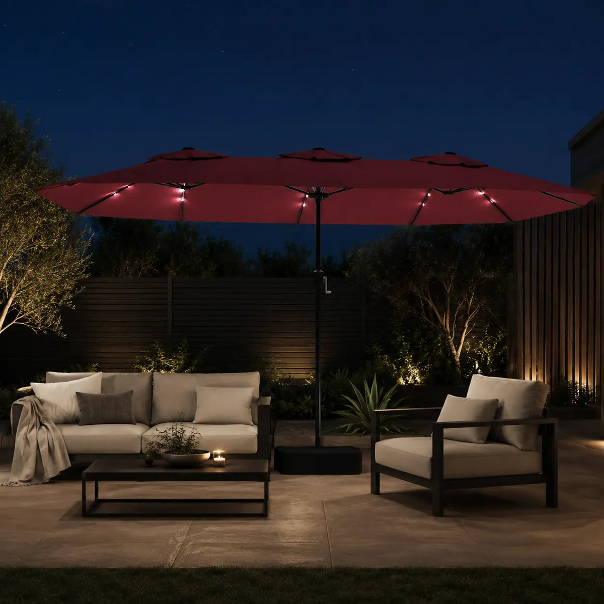 Large bordeaux double canopy market umbrella with LED lights over an outdoor lounge area in a garden setting at night