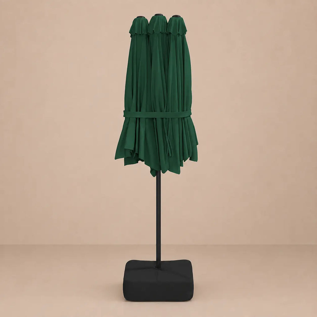 Green double canopy market umbrella folded closed on black aluminium pole with square weighted base