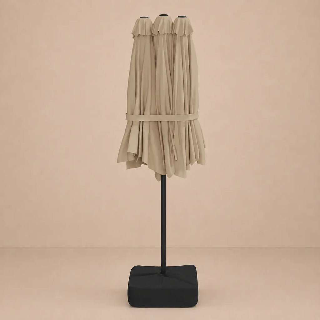 Taupe double canopy market umbrella folded closed on black aluminium pole with square weighted base