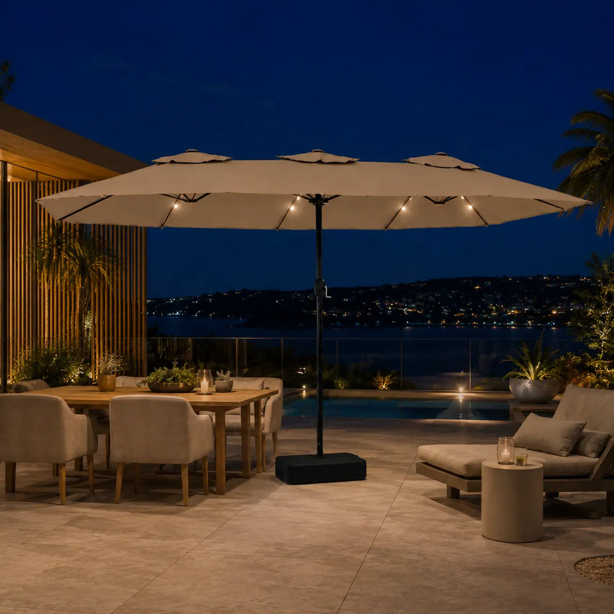Large taupe double canopy market umbrella with LED lights over an outdoor dining and lounge area at night with coastal city views