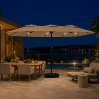 Large taupe double canopy market umbrella with LED lights over an outdoor dining and lounge area at night with coastal city views