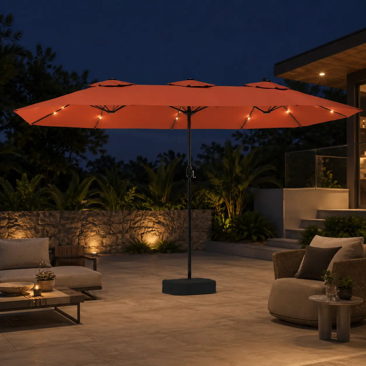 Large terracotta double canopy market umbrella with LED lights over an outdoor lounge area in a garden setting at night