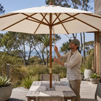 Man opening the rope-and-pulley mechanism of the 3m sand market umbrella on a coastal timber deck in Australia