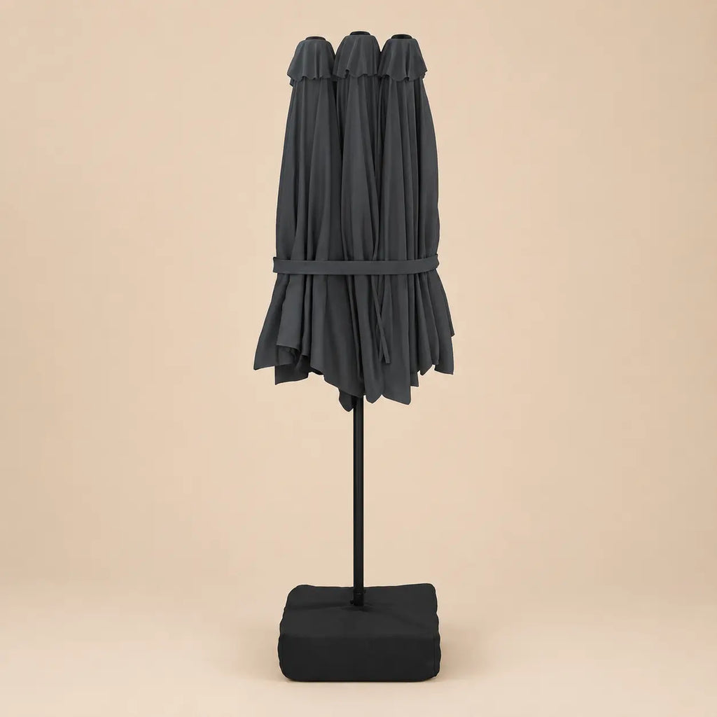 Anthracite double canopy market umbrella folded closed on black aluminium pole with square weighted base