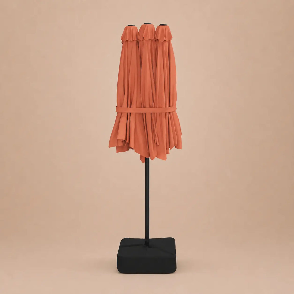 Terracotta double canopy market umbrella folded closed on black aluminium pole with square weighted base