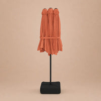 Terracotta double canopy market umbrella folded closed on black aluminium pole with square weighted base