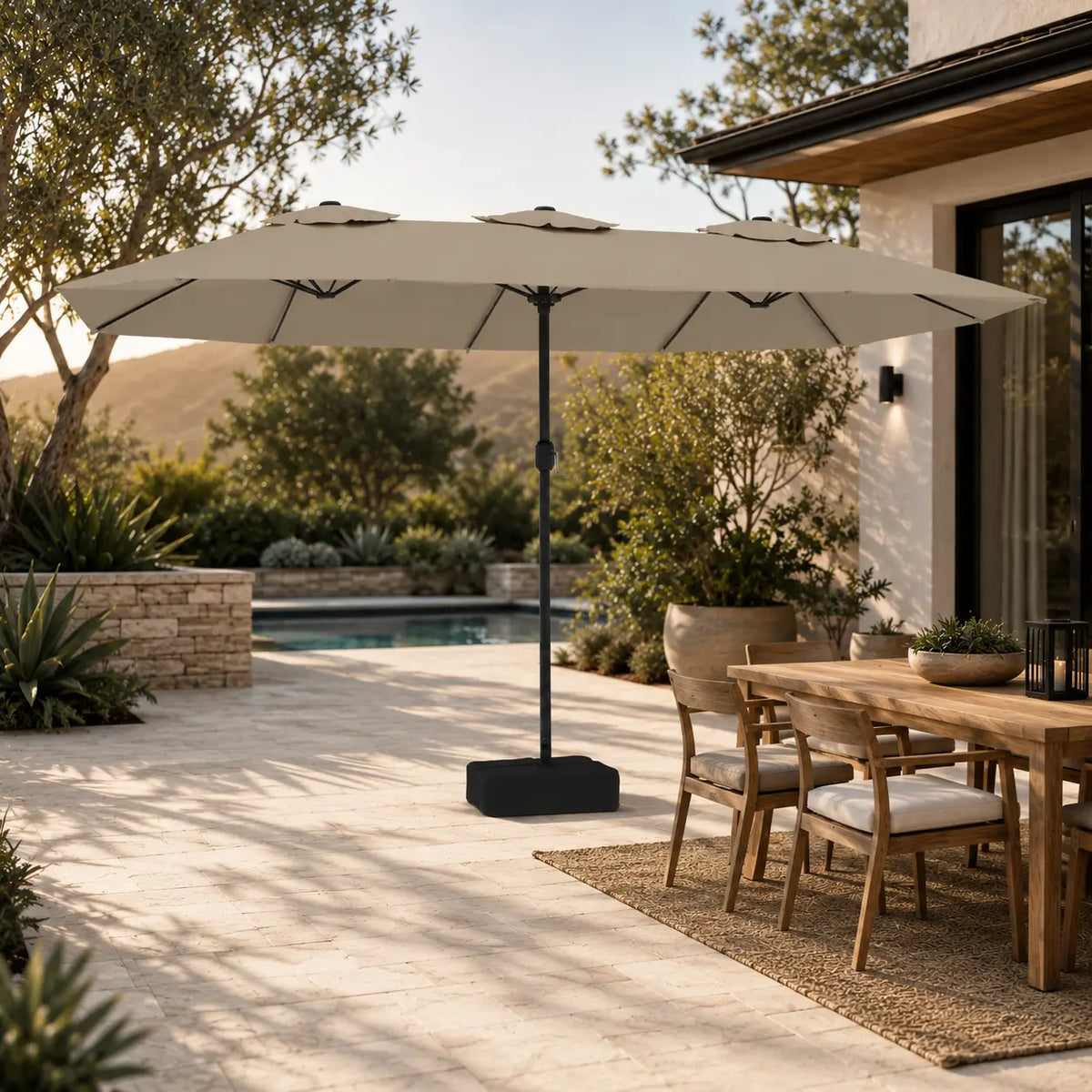 4.5m taupe double canopy market umbrella shading a timber outdoor dining table in a garden alfresco setting beside a pool