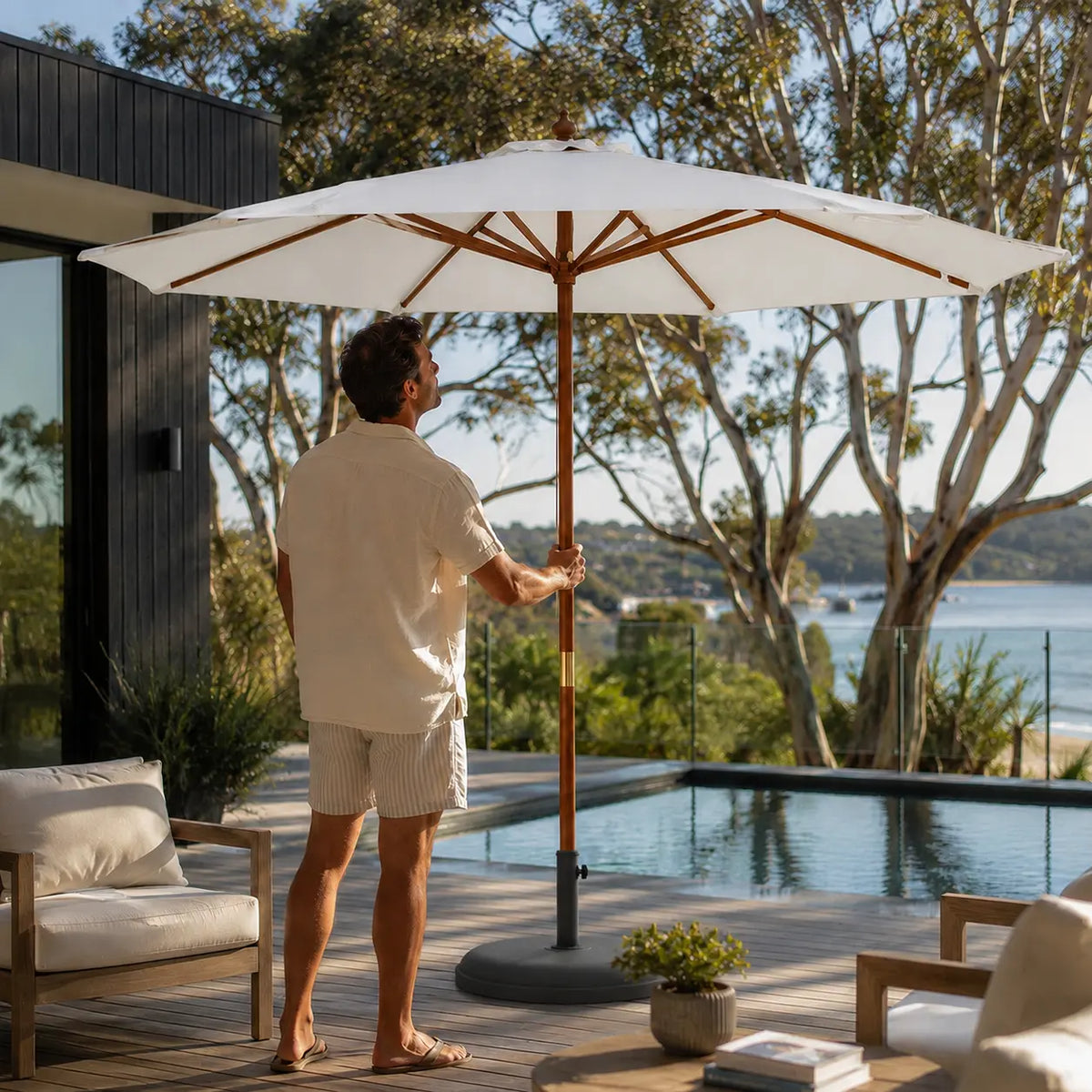 Man opening the 3.5m large market umbrella on a timber deck overlooking a coastal waterway in Australia