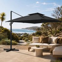 Black rectangular cantilever umbrella shading an outdoor lounge on a coastal timber deck with ocean view
